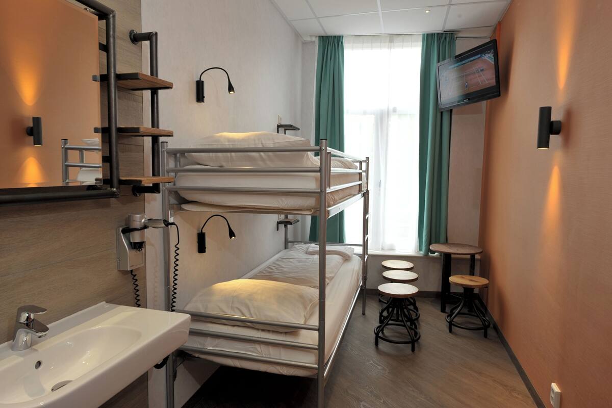 A hotel room with bunk beds, a sink, a TV, and two stools.