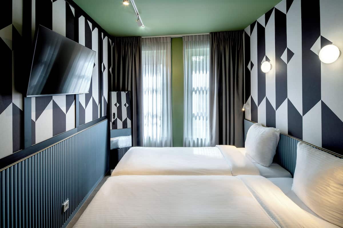 A hotel room with a bed, a TV, and a window with curtains.