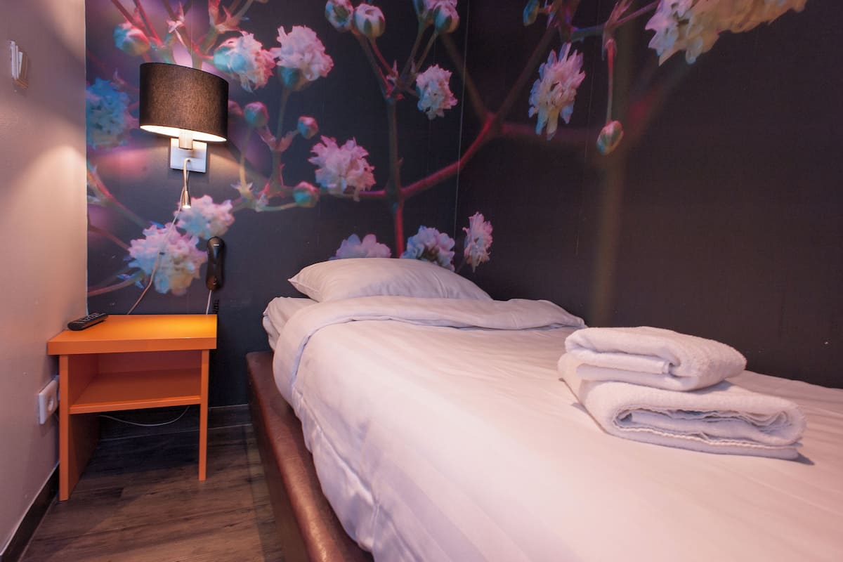 A hotel room with a bed, a nightstand, a lamp, and a wall with a floral mural.