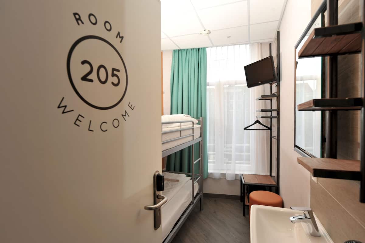 A compact hotel room with bunk beds, a small table, a sink, and a TV mounted on the wall.