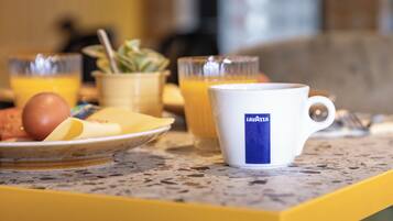 A breakfast setting with a plate of eggs, a bowl of fruit, and a mug labeled "Lavazza" on a speckled countertop.
