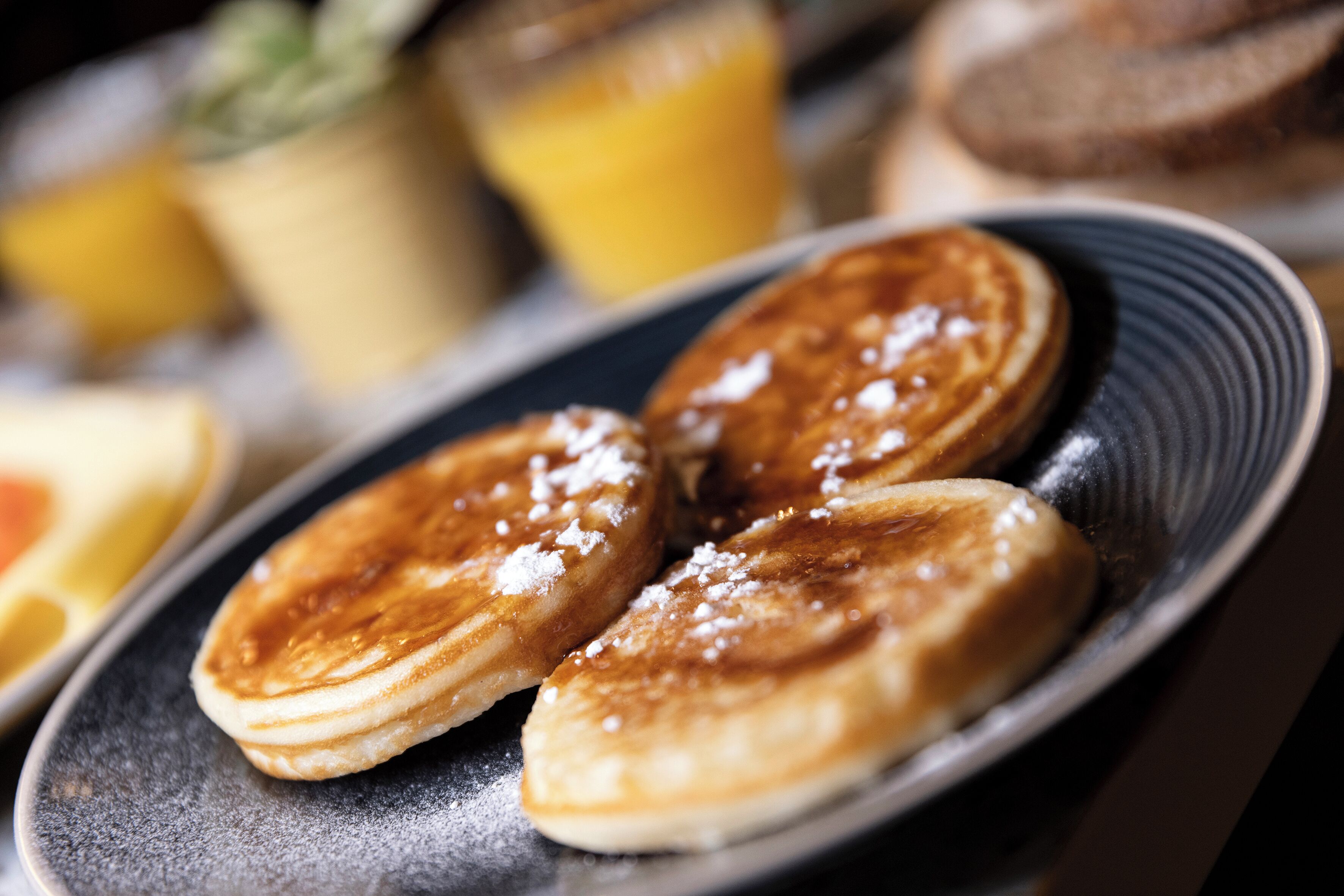 A plate of pancakes with powdered sugar, accompanied by a glass of orange juice and a cup of coffee.