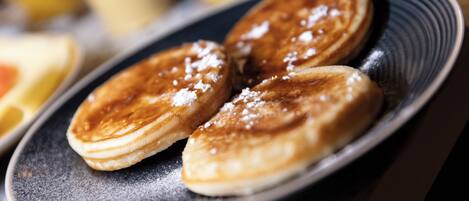 A plate of pancakes with powdered sugar, accompanied by a glass of orange juice and a cup of coffee.