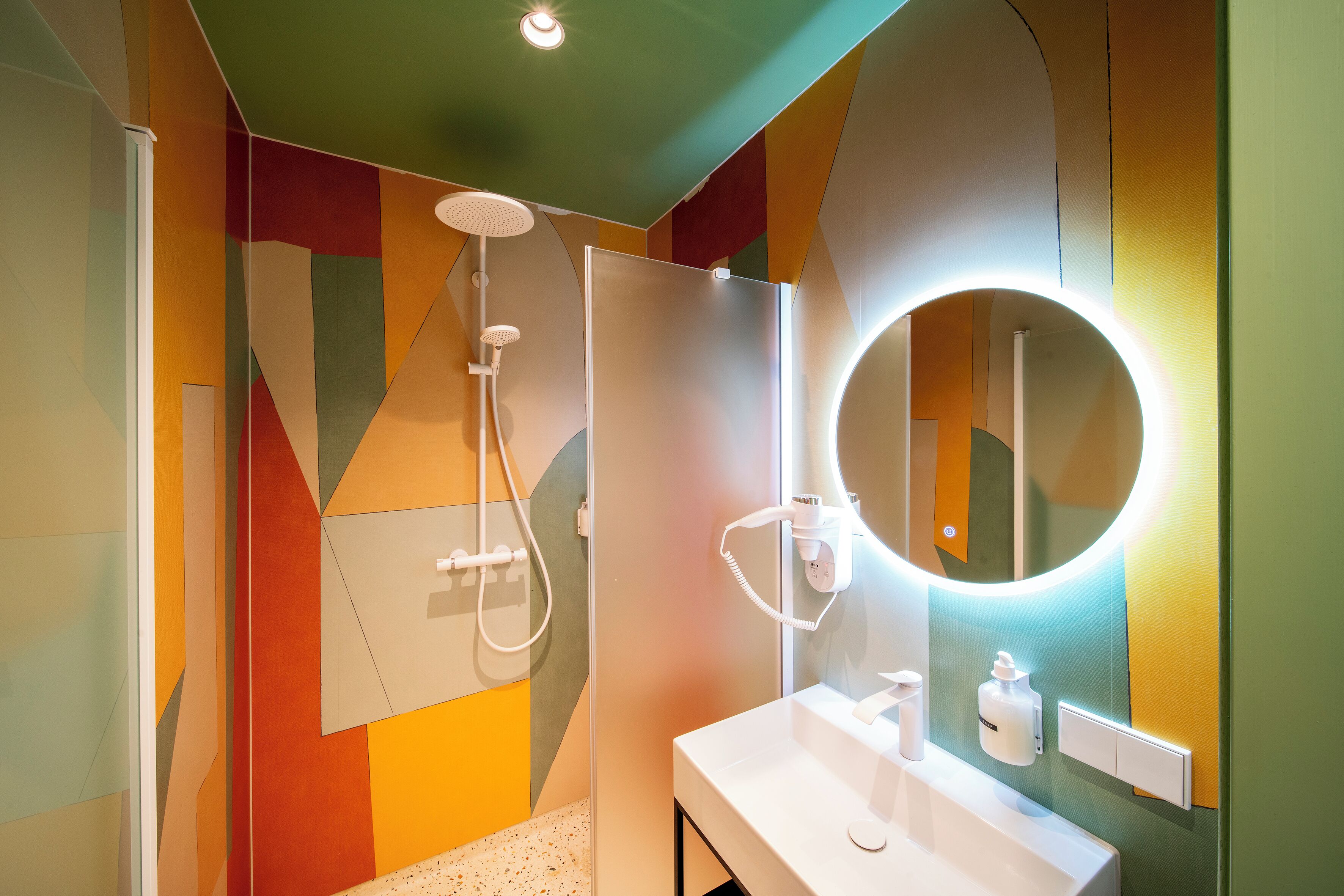 A bathroom with a modern design, featuring a shower, a sink, and a mirror with a circular light.