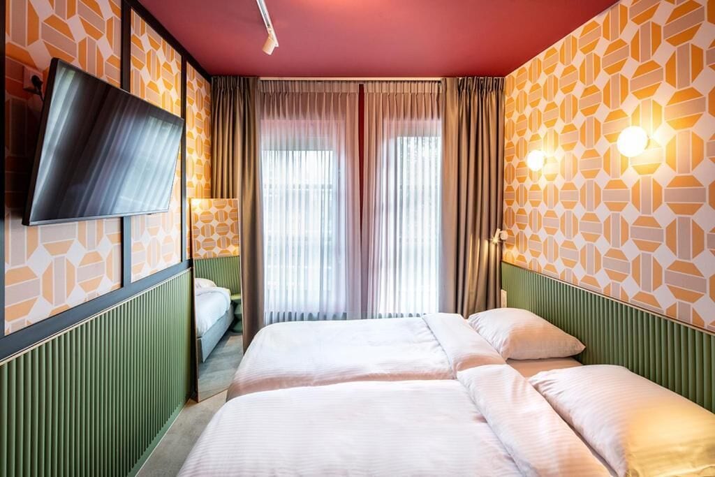 Une chambre d’hôtel avec deux lits, un téléviseur à écran plat et une grande fenêtre avec des rideaux.