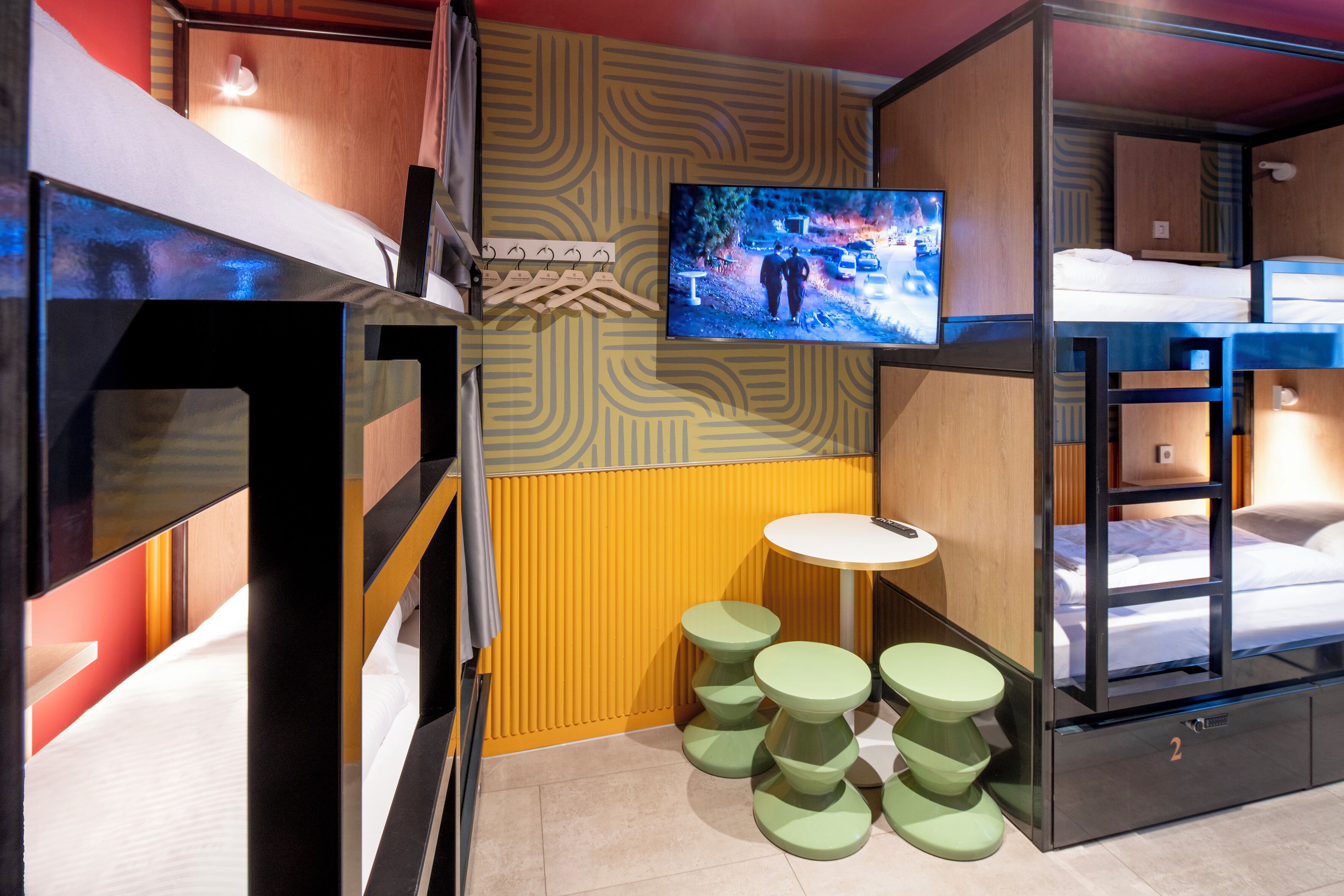 Una habitación pequeña con literas, televisor y una mesita redonda con taburetes.