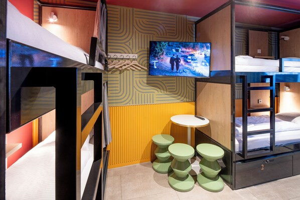 A compact room with bunk beds, a television, and a small round table with stools.