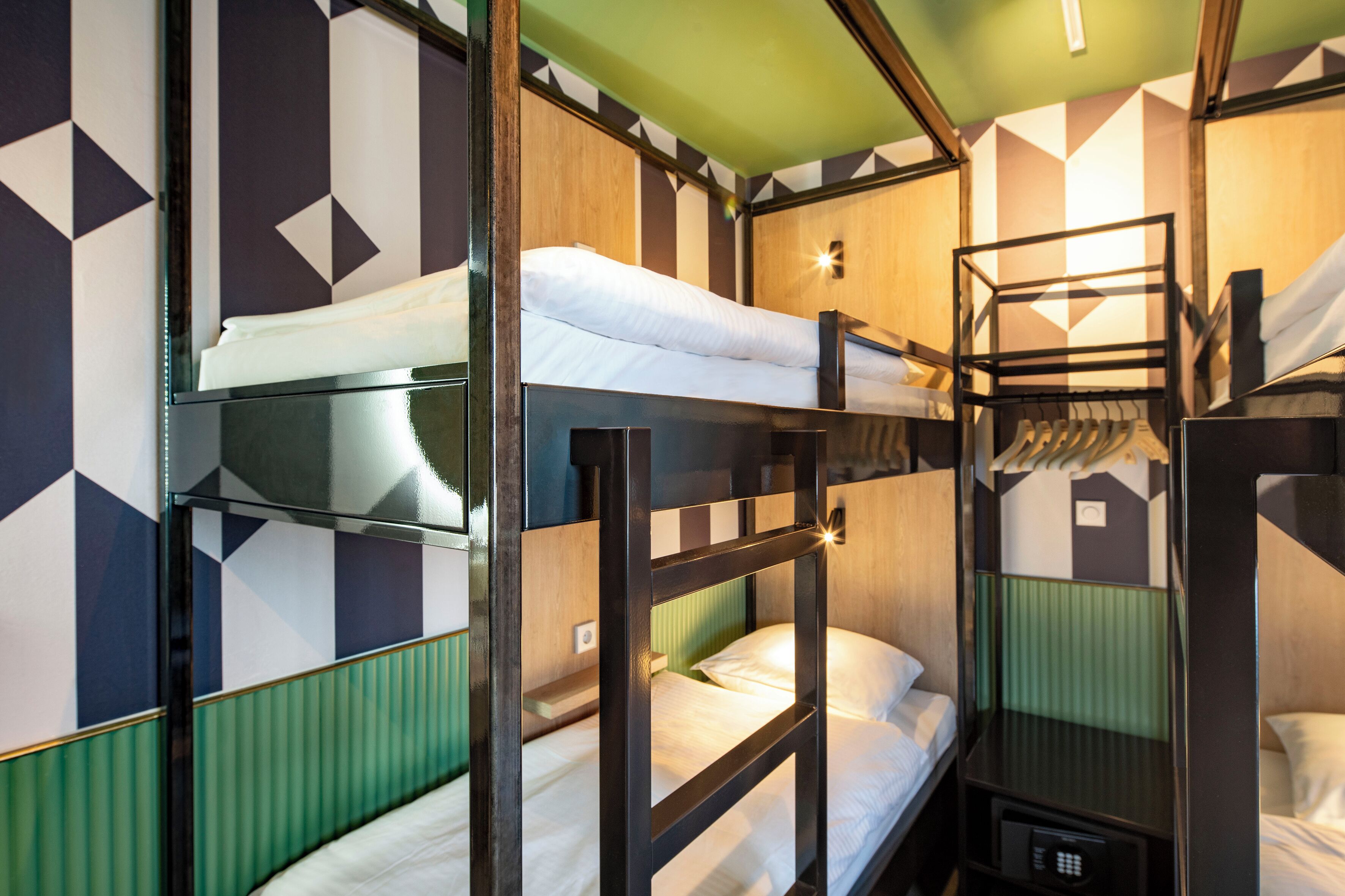 A bunk bed room with a geometric patterned wall, a green accent wall, and a small bedside table with a lamp.