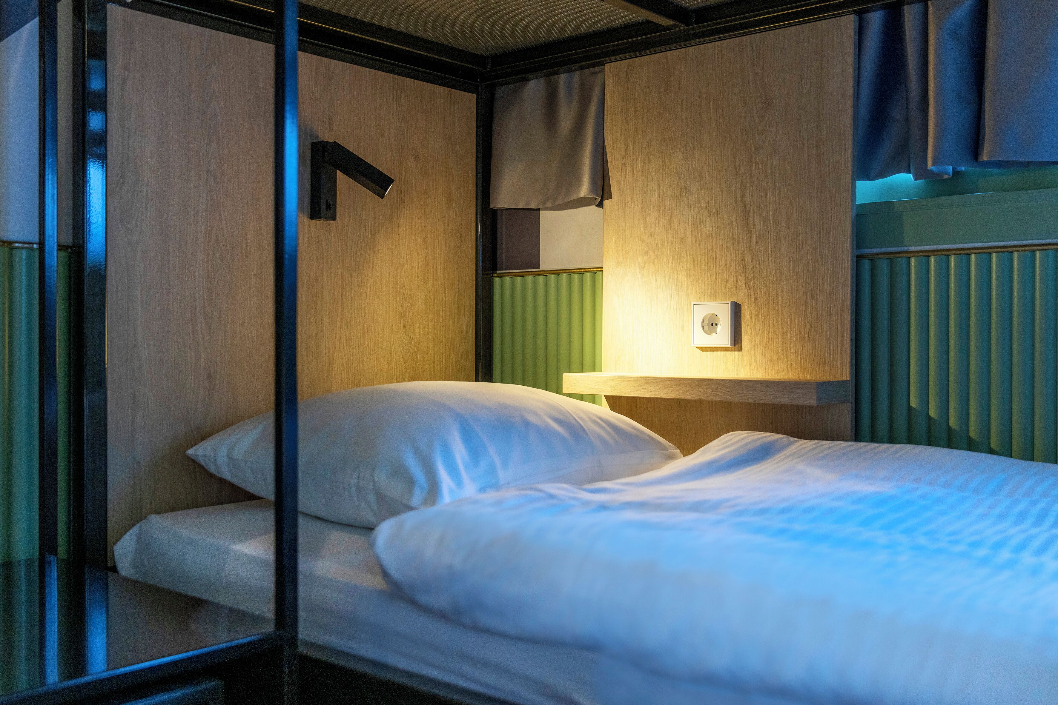 Ein Einzelbett mit weißer Bettwäsche in einem Zimmer mit Holzwänden und einem grünen Heizkörper.