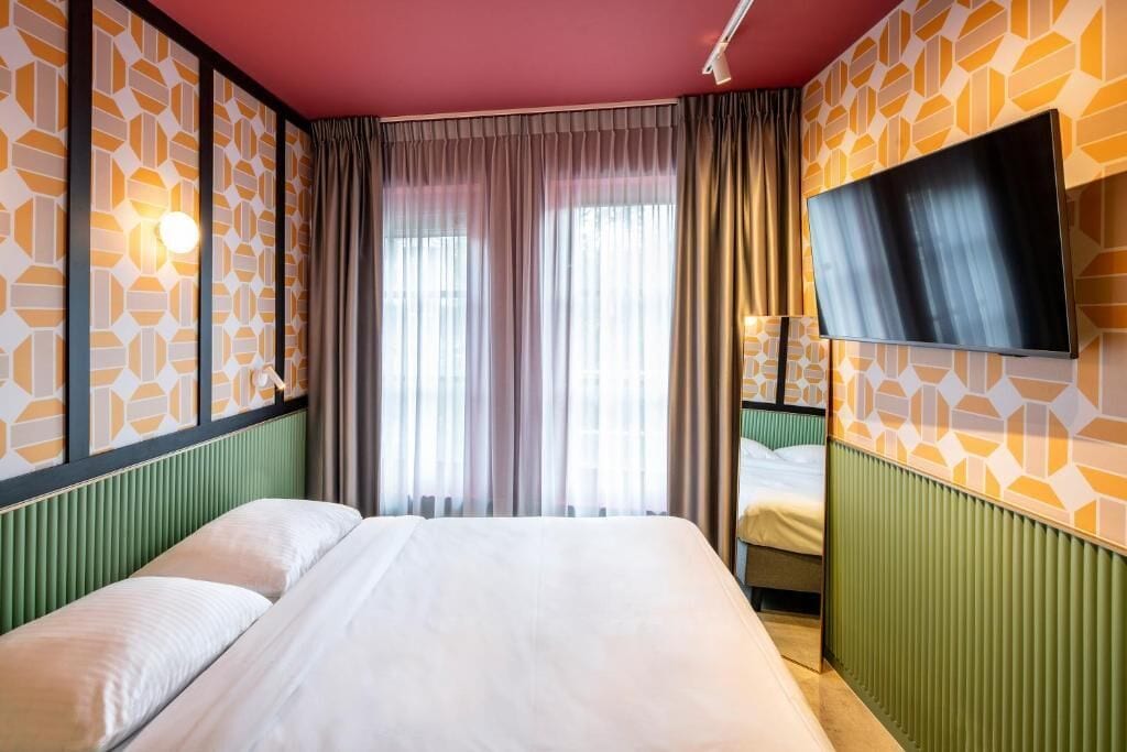 Una habitación de hotel con una cama grande, un televisor de pantalla plana en la pared y papel tapiz estampado.