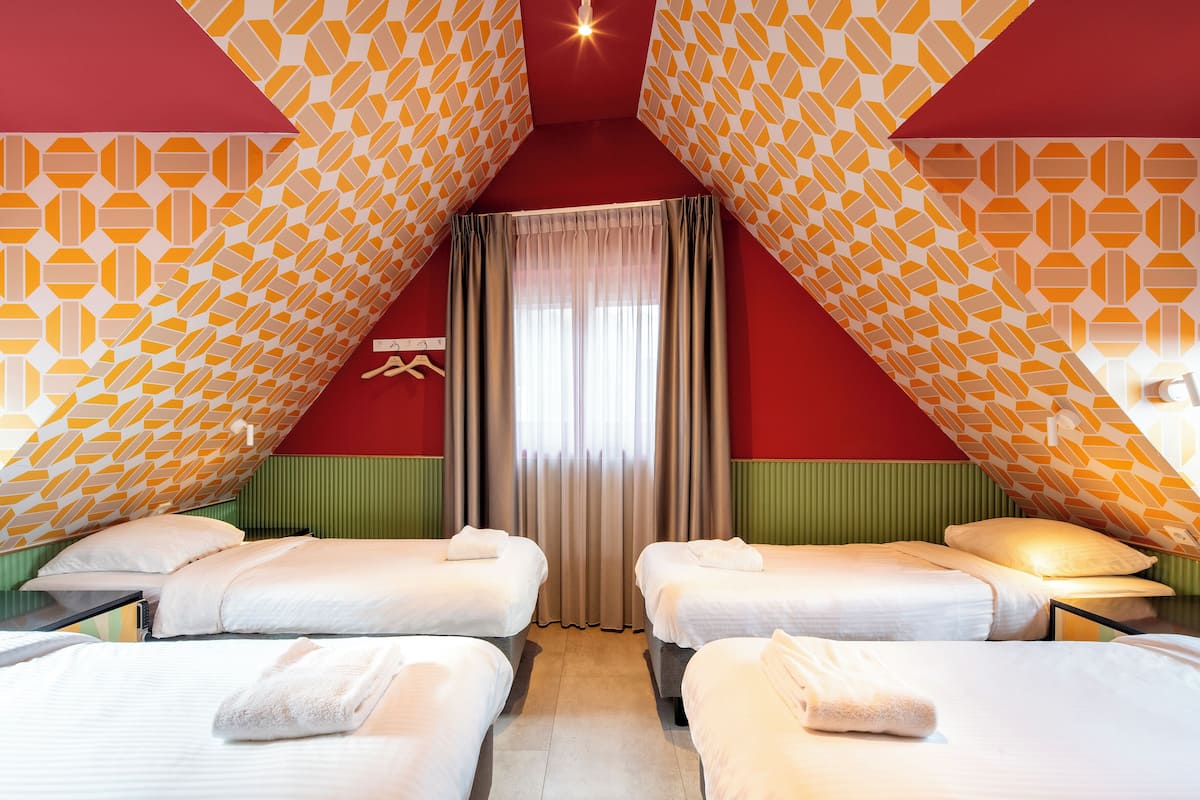 A room with two beds, a window with curtains, and patterned walls.