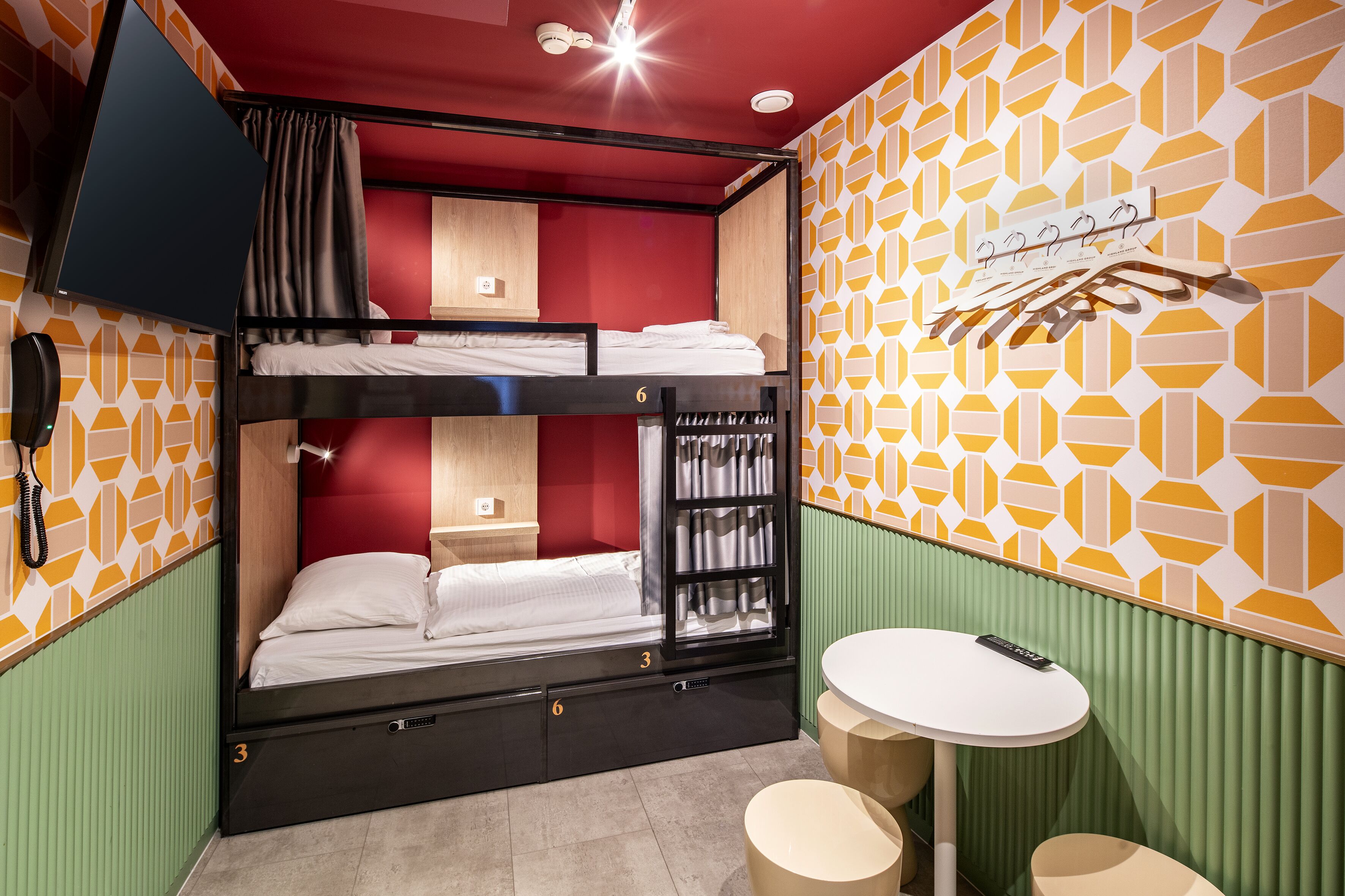 A bunk bed room with a small table and a hanging coat rack.
