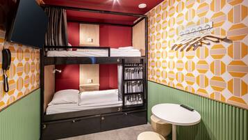 A bunk bed room with a small table and a hanging coat rack.