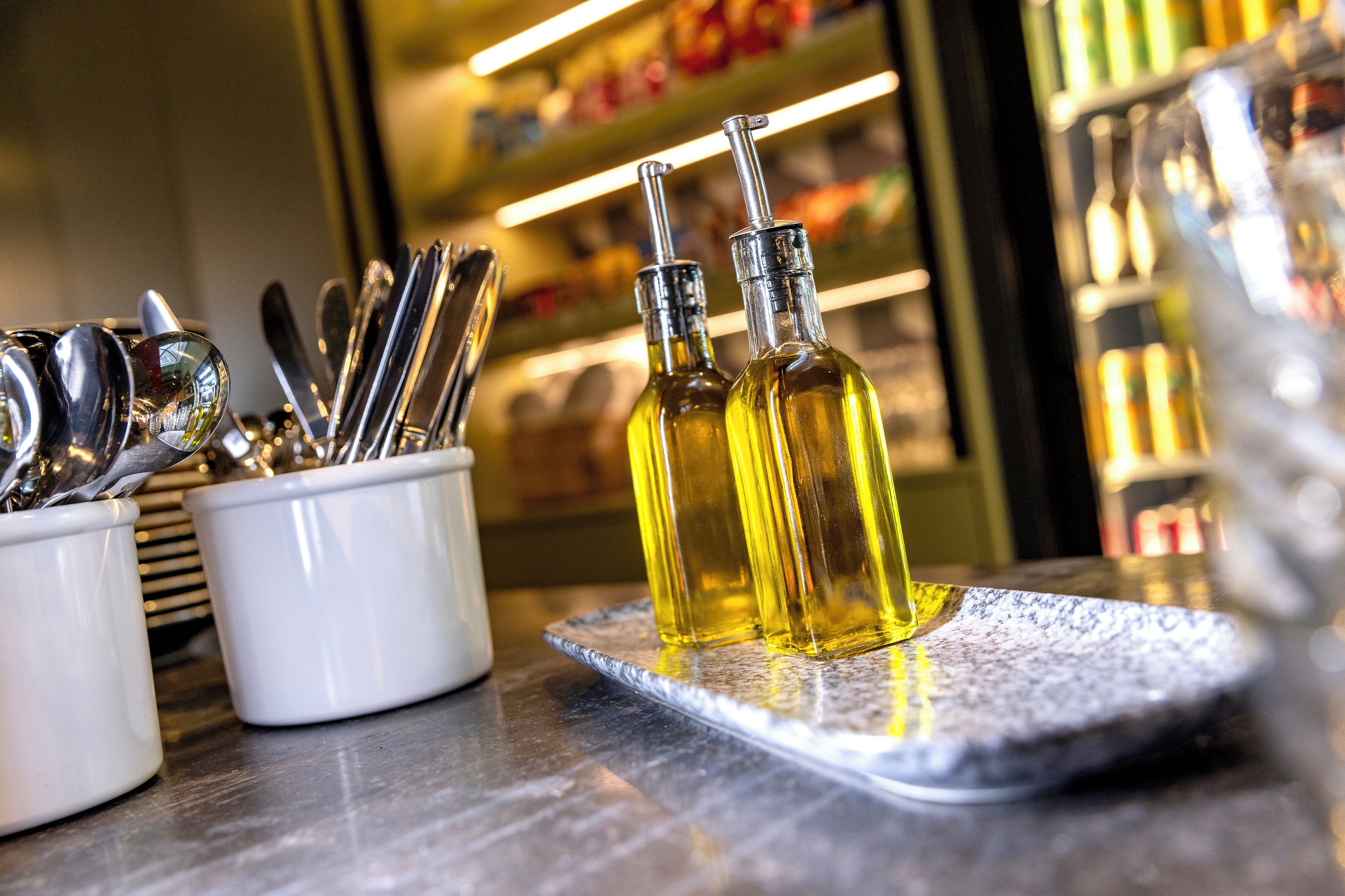 A bar area with a marble countertop, a white container holding utensils, and two bottles of olive oil.