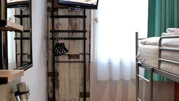 Een hotelkamer met een stapelbed, een televisie bevestigd aan een houten wand, een klein tafeltje met een afstandsbediening, en een wastafel.