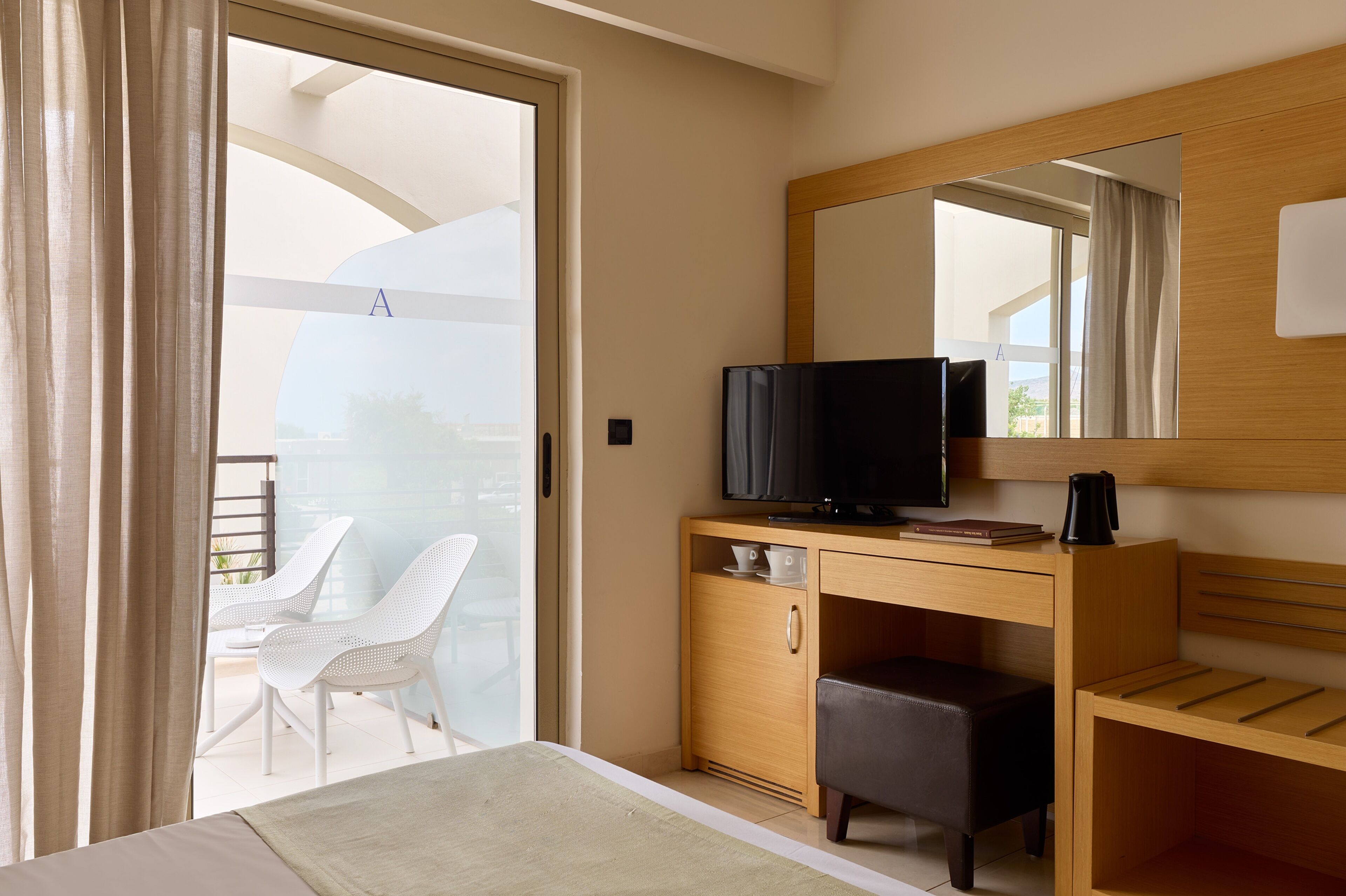 Una habitación de hotel con cama, televisión, escritorio de madera, silla y balcón con vistas.