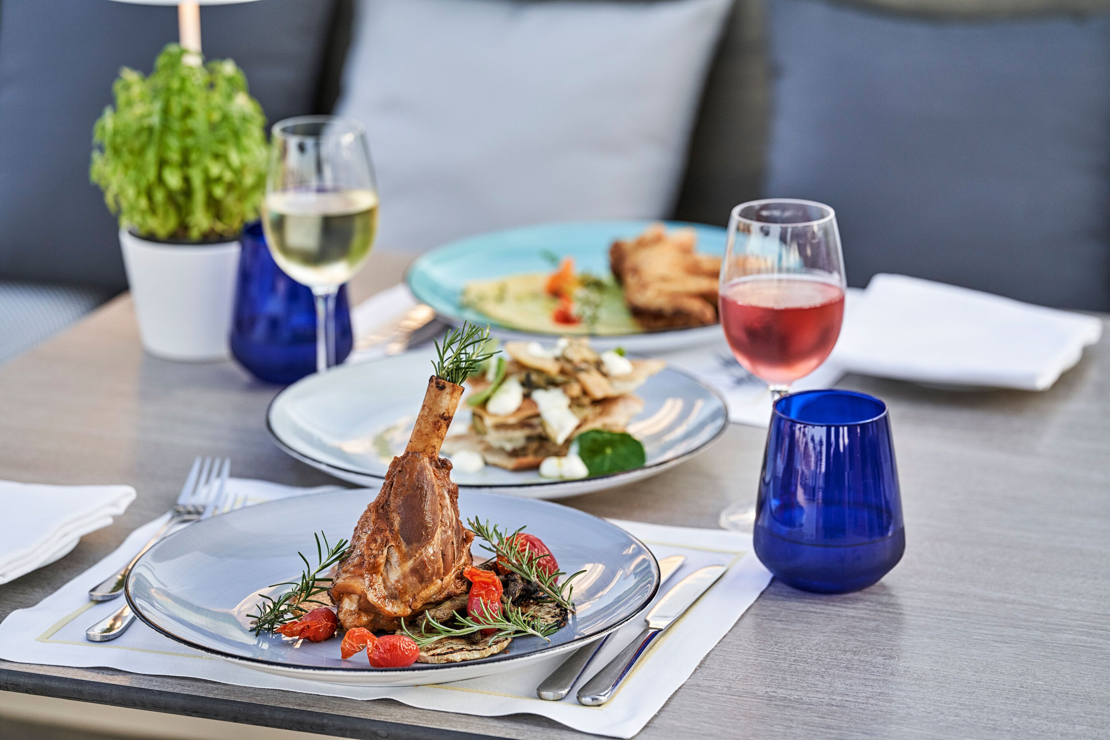 A dining table with plates of food, wine glasses, and cutlery.