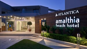Exterior del Hotel Amalthia Beach, con un diseño moderno, que destaca un letrero llamativo y jardines bien cuidados.