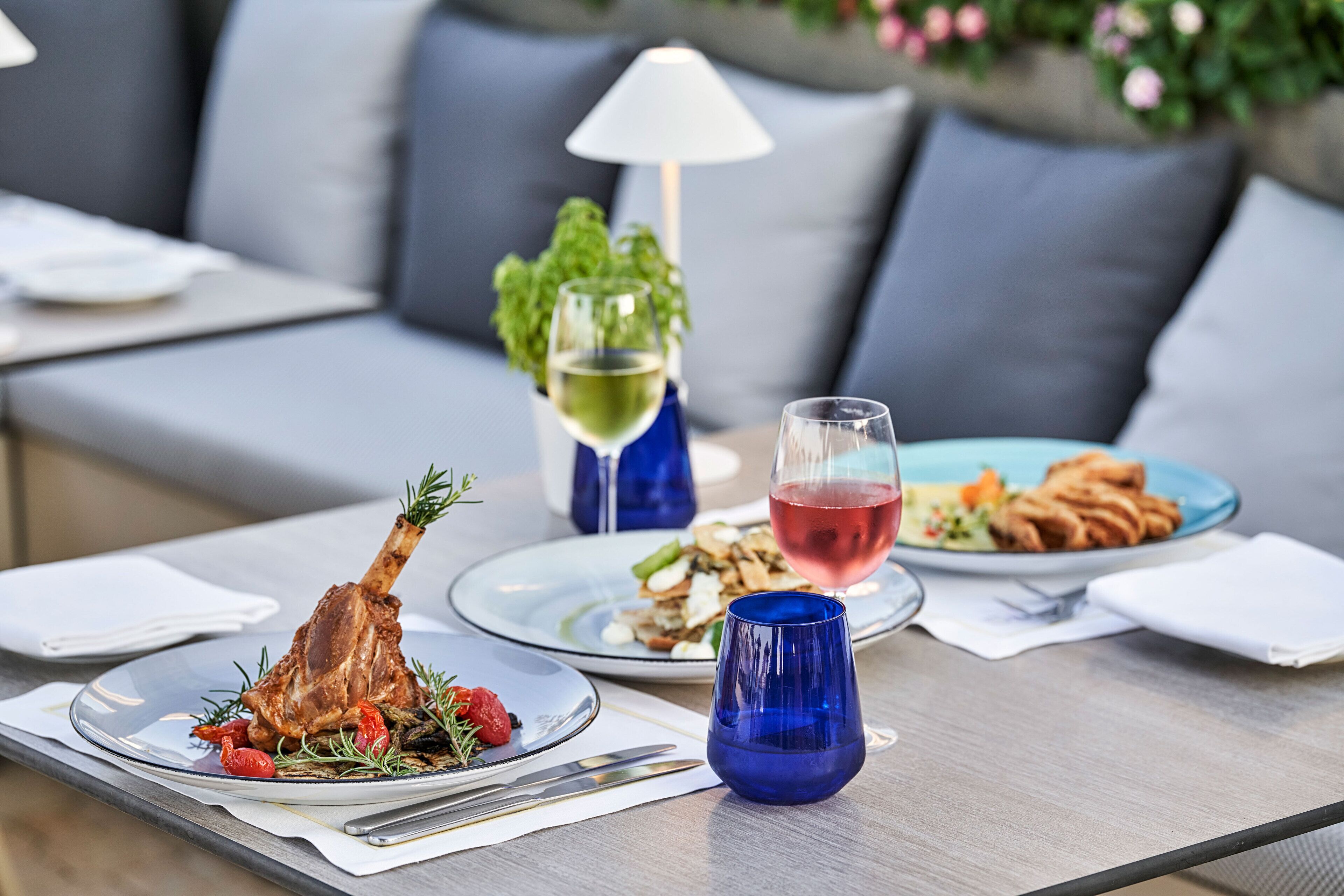 Una mesa de comedor con platos de comida, una copa de vino y un vaso azul.