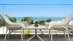 Un balcón con dos sillas blancas y una mesita pequeña, con vistas panorámicas al mar y la vegetación.