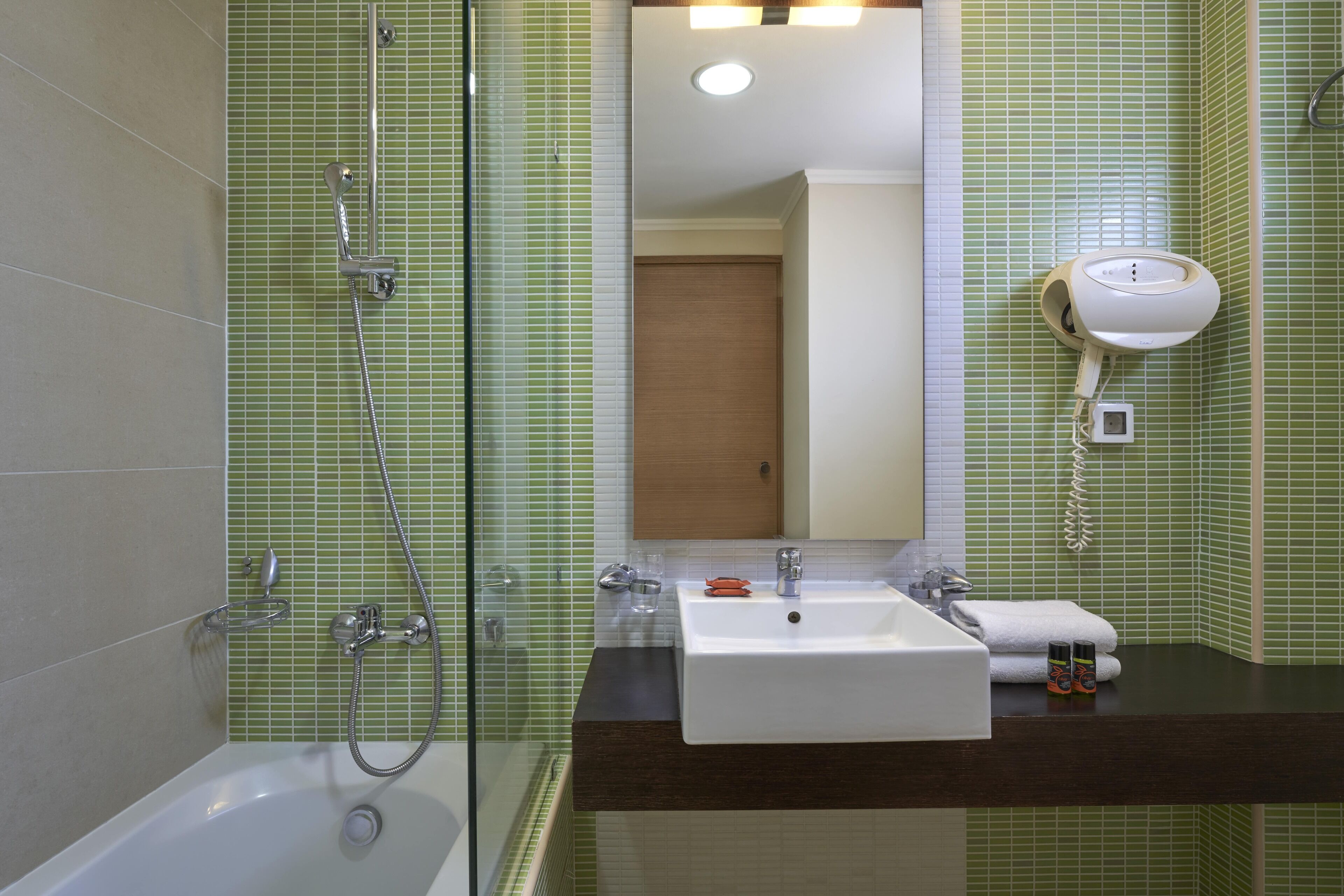 Un baño con bañera, ducha, lavamanos y secador de pelo fijado a la pared.