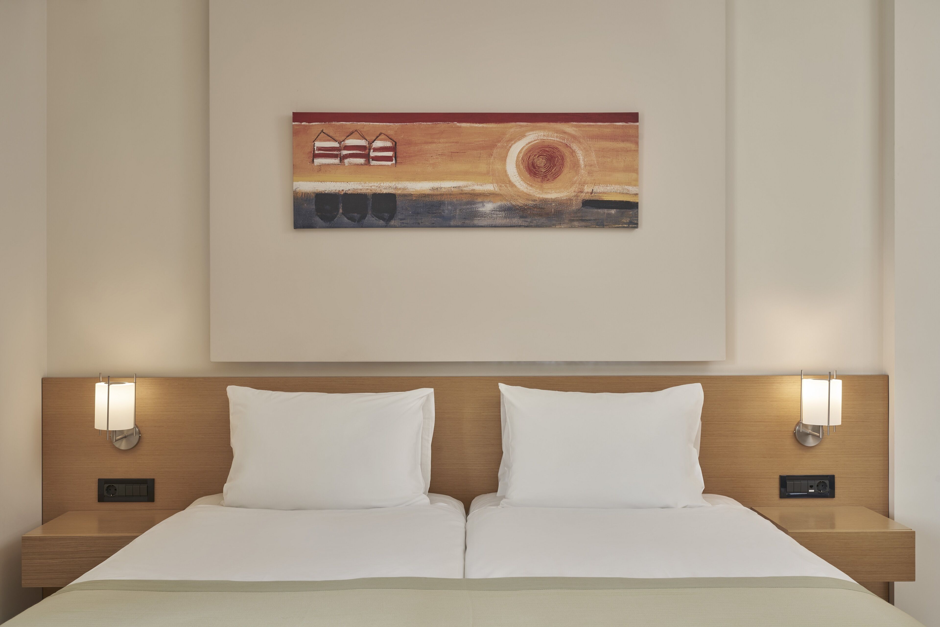 Une chambre d’hôtel avec un lit double, deux tables de chevet, une œuvre d’art accrochée au mur et deux appliques murales.