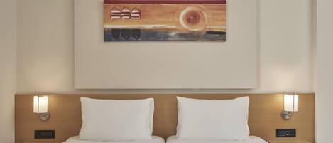 A hotel room with a double bed, two bedside tables, a wall-mounted artwork, and two wall-mounted light fixtures.