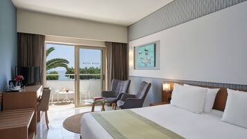 Habitació d'hotel amb un llit gran, escriptori amb televisió, una cadira, taula petita amb un llibre i vista al mar a través de les portes del balcó.