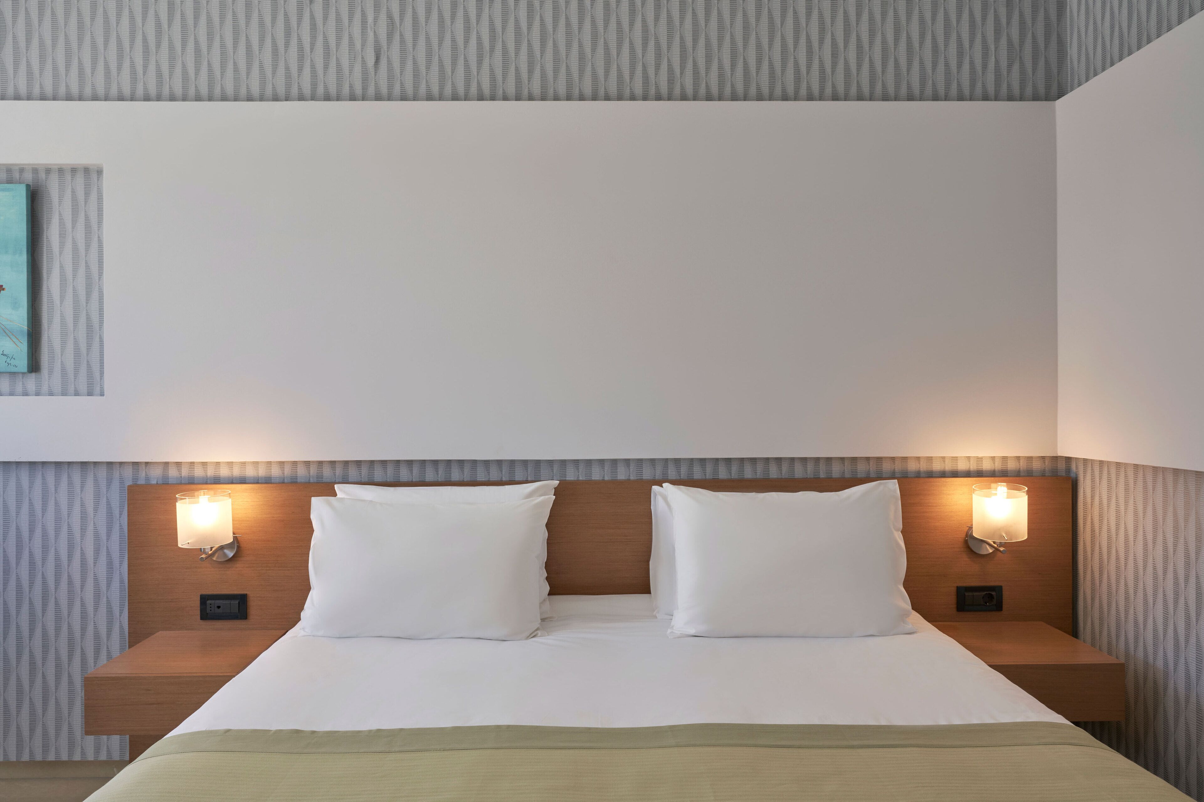 A hotel room with a neatly made bed, two bedside tables with lamps, and a patterned wall.