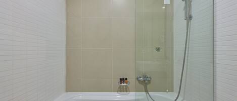 A modern bathroom with a glass-enclosed shower, a white bathtub, and a small shelf with toiletries.