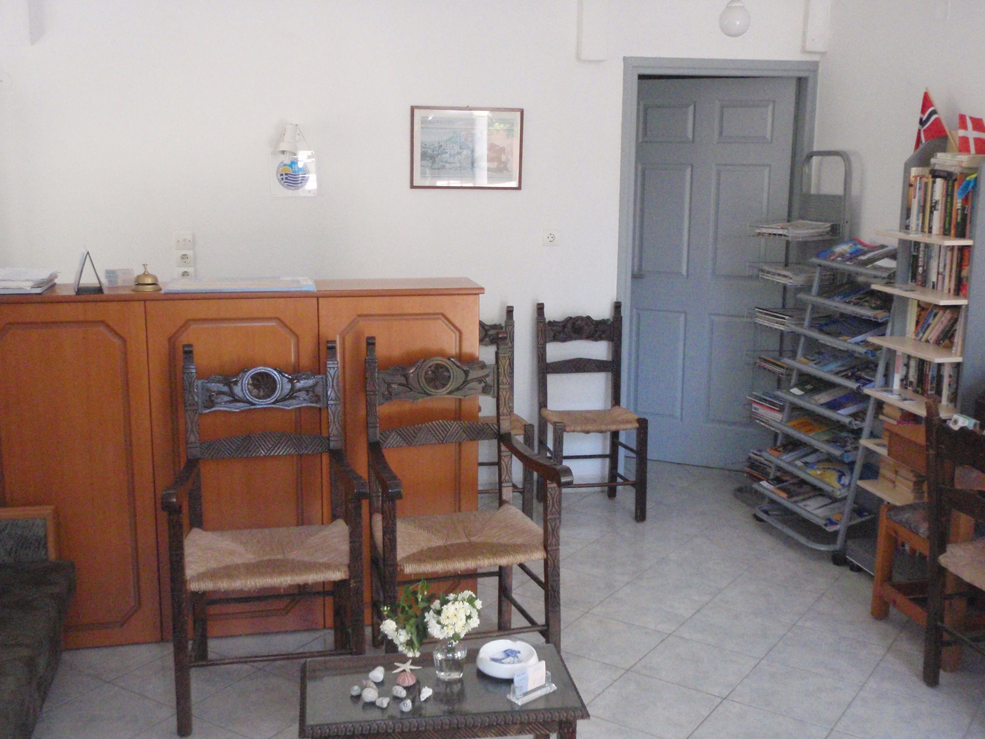 A room with two wooden chairs, a small table with a vase and decorative items, a bookshelf filled with books, and a door with a small shelf above it.