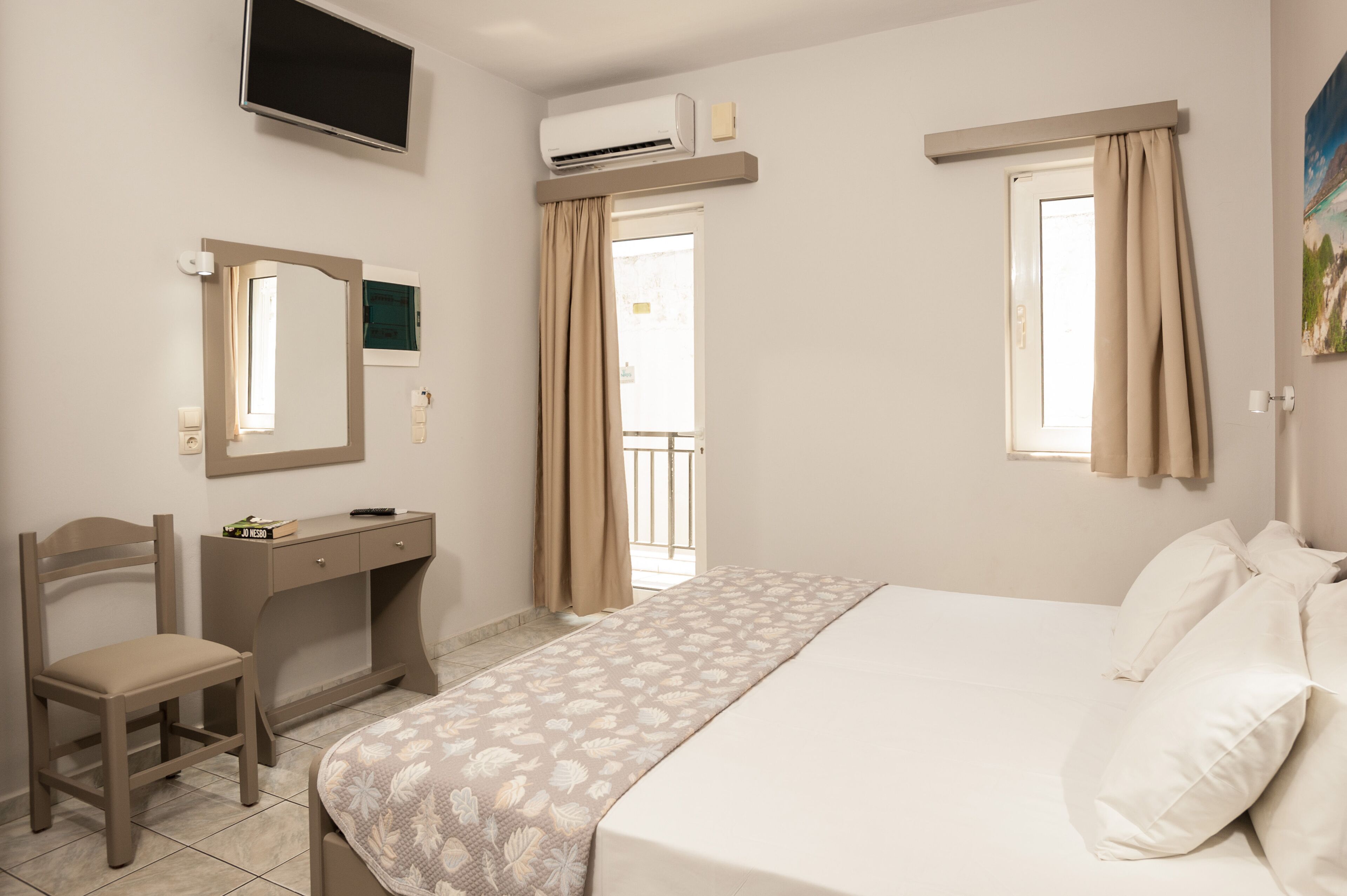 A hotel room with a bed, a desk, a chair, a TV, and a window with curtains.