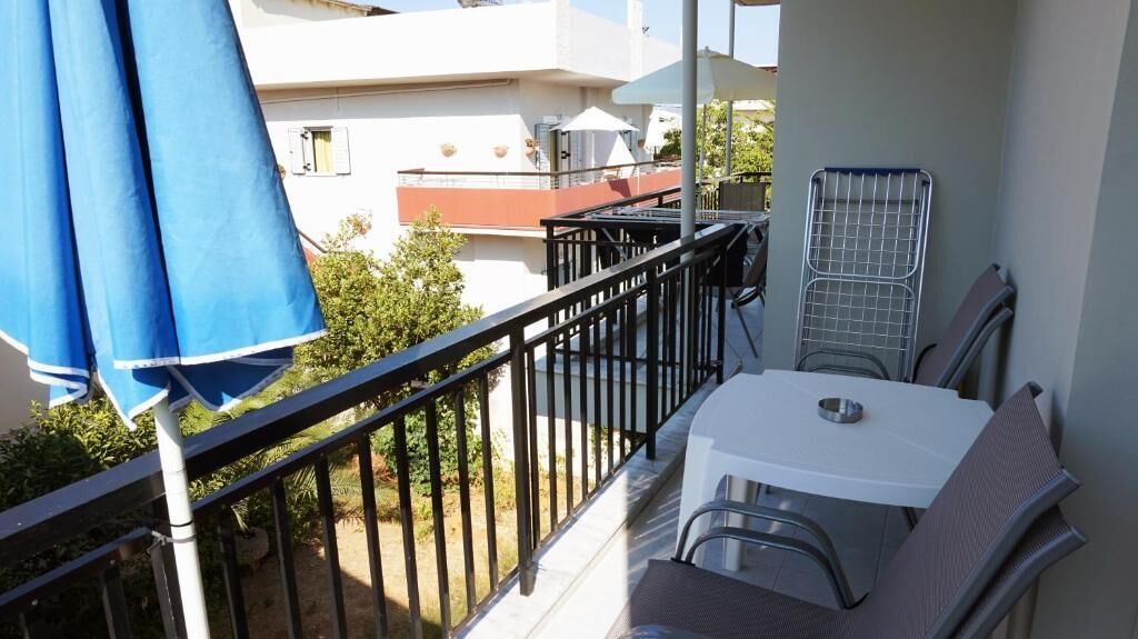 Un balcón con mesa y sillas, una silla de metal y un paraguas azul.