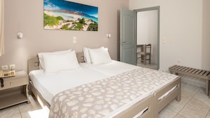 A bedroom with a large bed, a bedside table with a lamp, a chair, and a bench. - Niriis Hotel (Chania)