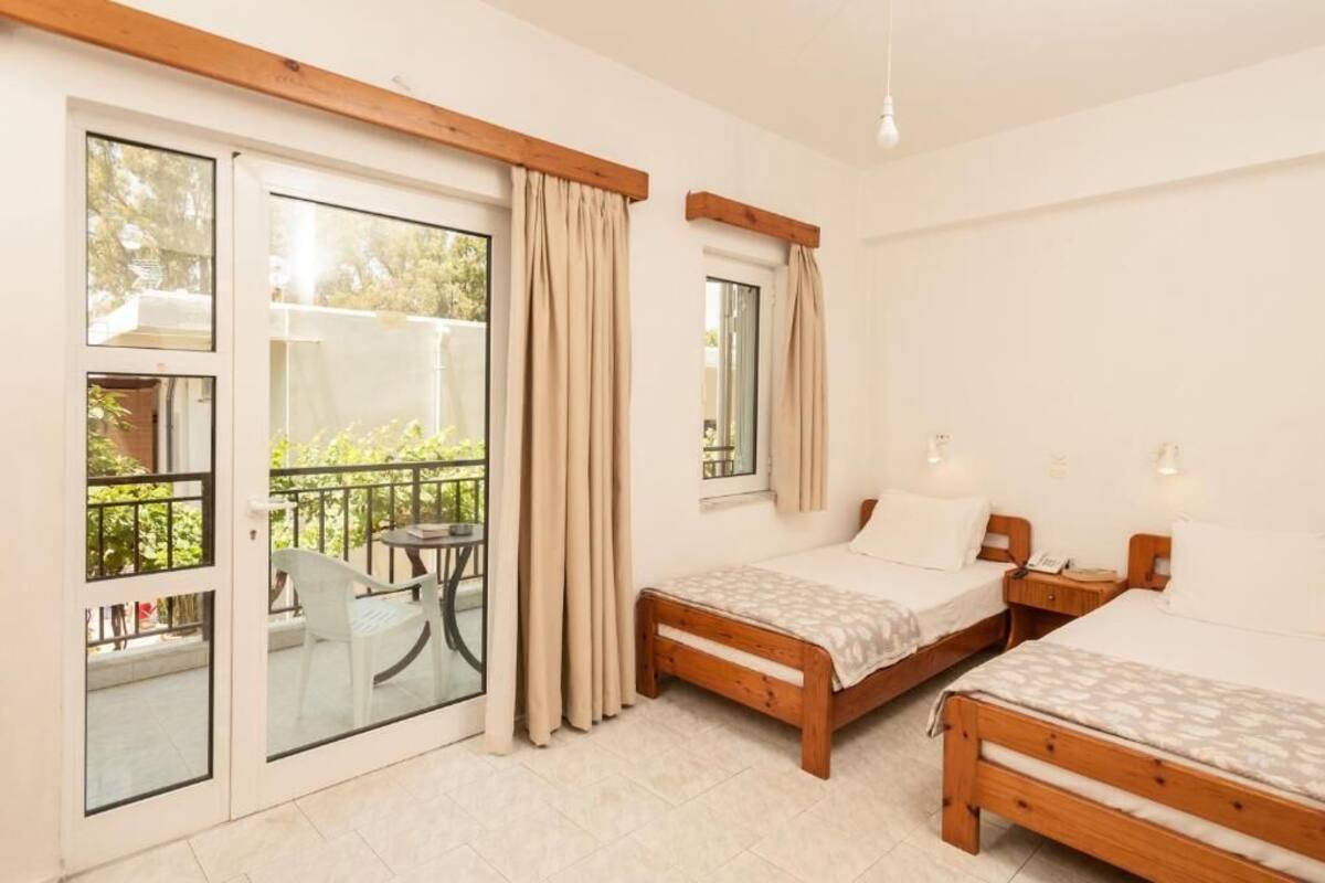A bedroom with two wooden beds, a balcony with a table and chairs, and a window with curtains.