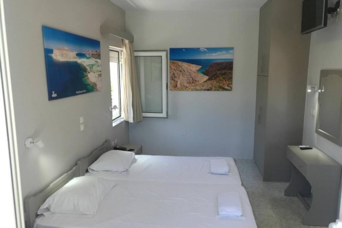A bedroom with two beds, a TV, and two paintings of coastal landscapes.