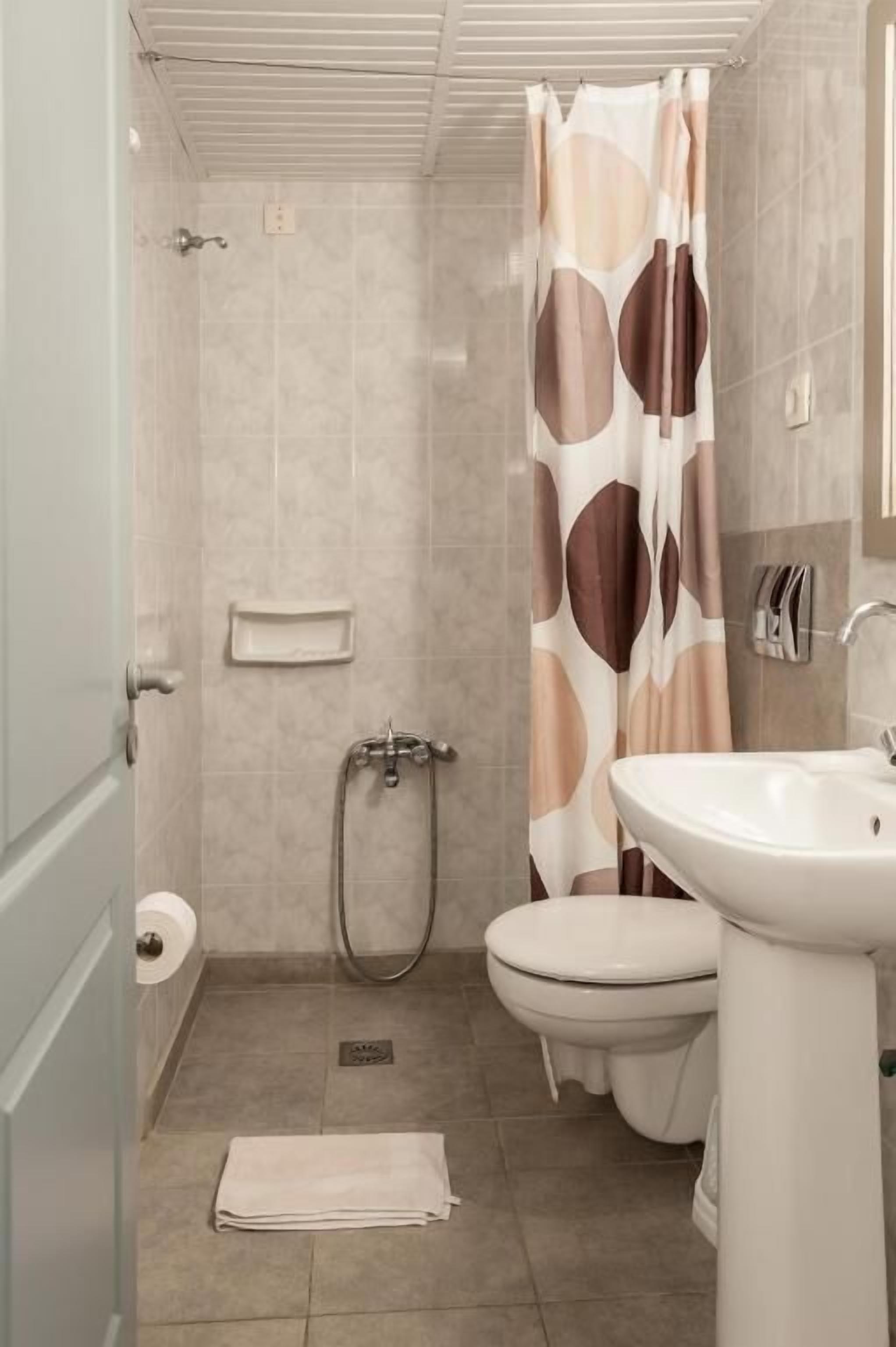 Een badkamer met een douche, toilet, wastafel en een handdoek op de vloer.