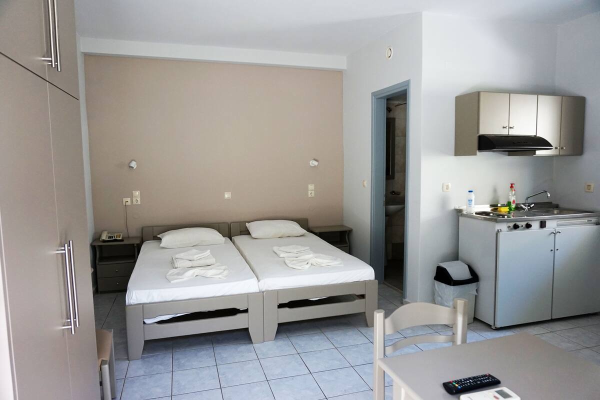 A hotel room with two beds, a kitchenette, a desk, and a chair.