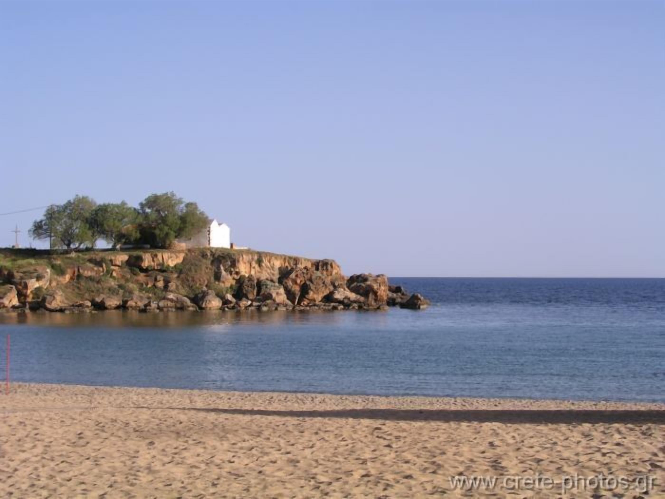 A coastal scene with a sandy beach, rocky cliffs, and a white building with trees.
