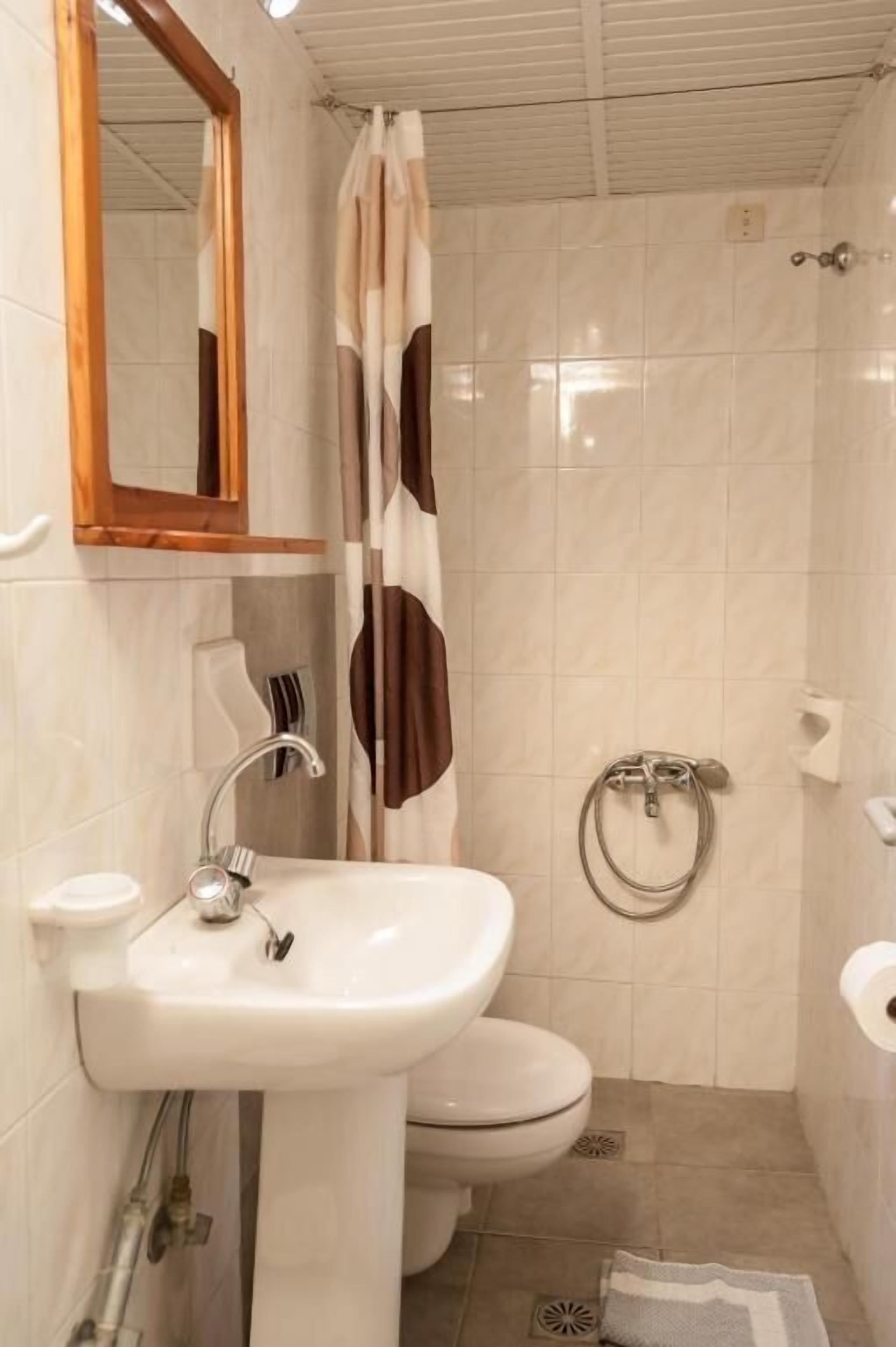 Een badkamer met een wastafel op een voetstuk, toilet en douche.
