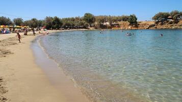 A beach with clear water, people swimming, and umbrellas on the sand.