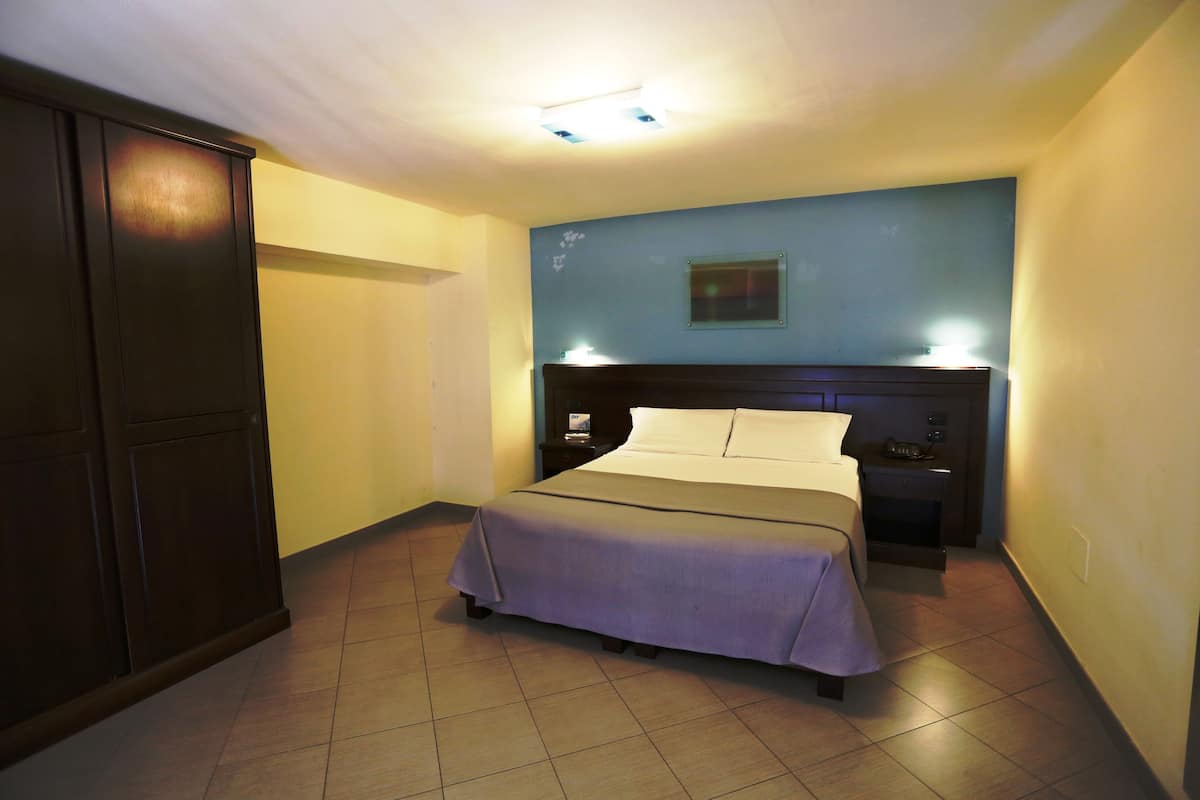 A hotel room with a bed, nightstand, and wardrobe.
