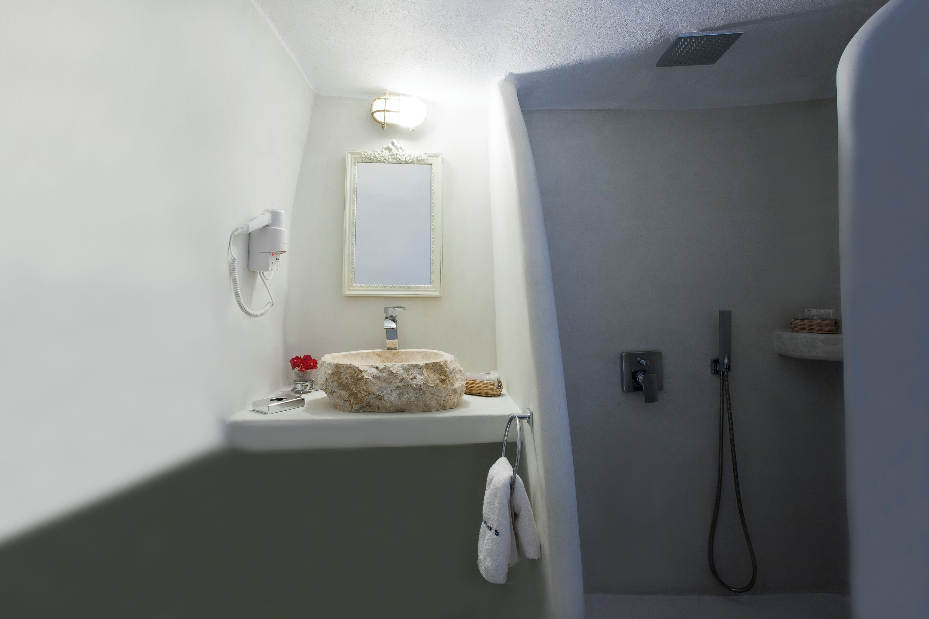 A bathroom with a stone sink, a mirror, a towel rack, and a shower.