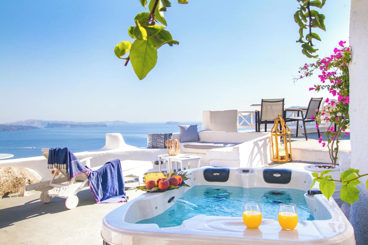 A hot tub with fruit and drinks, outdoor seating, and a view of the sea.