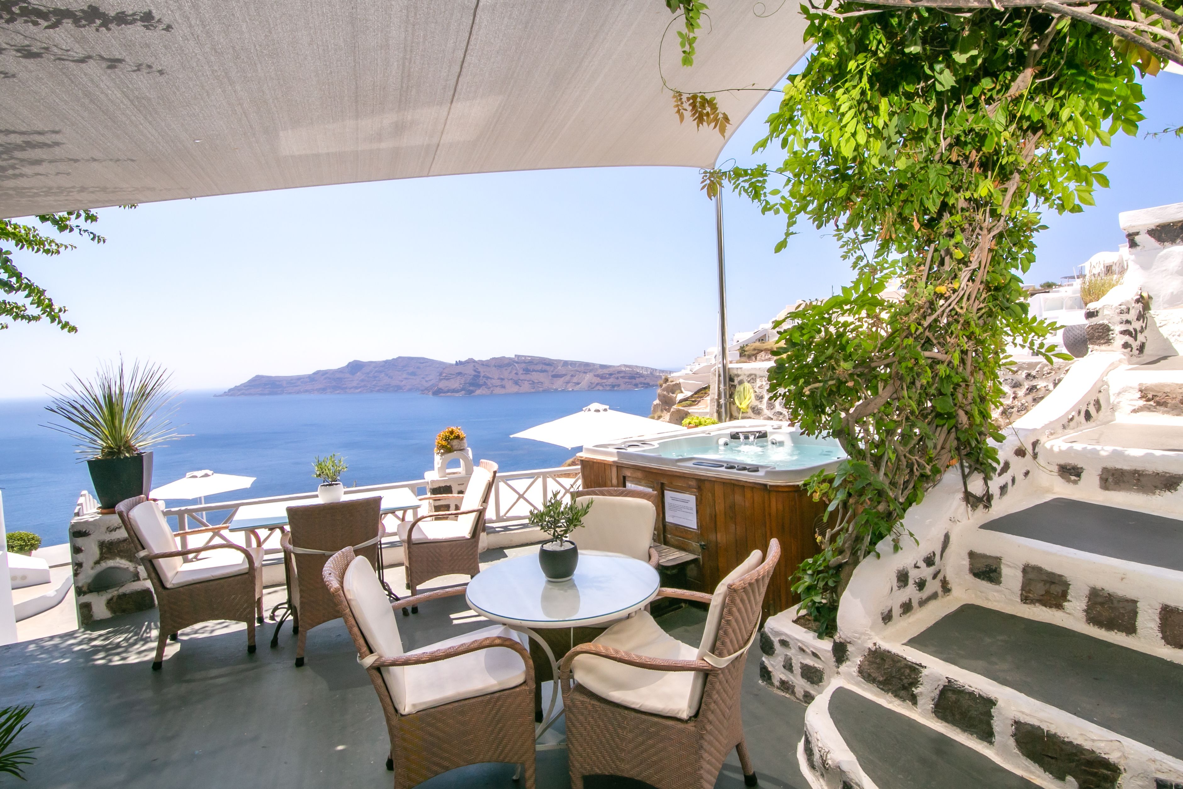 Un espace extérieur aménagé avec des chaises en osier et une table ronde, offrant une vue panoramique sur la mer et un paysage montagneux.