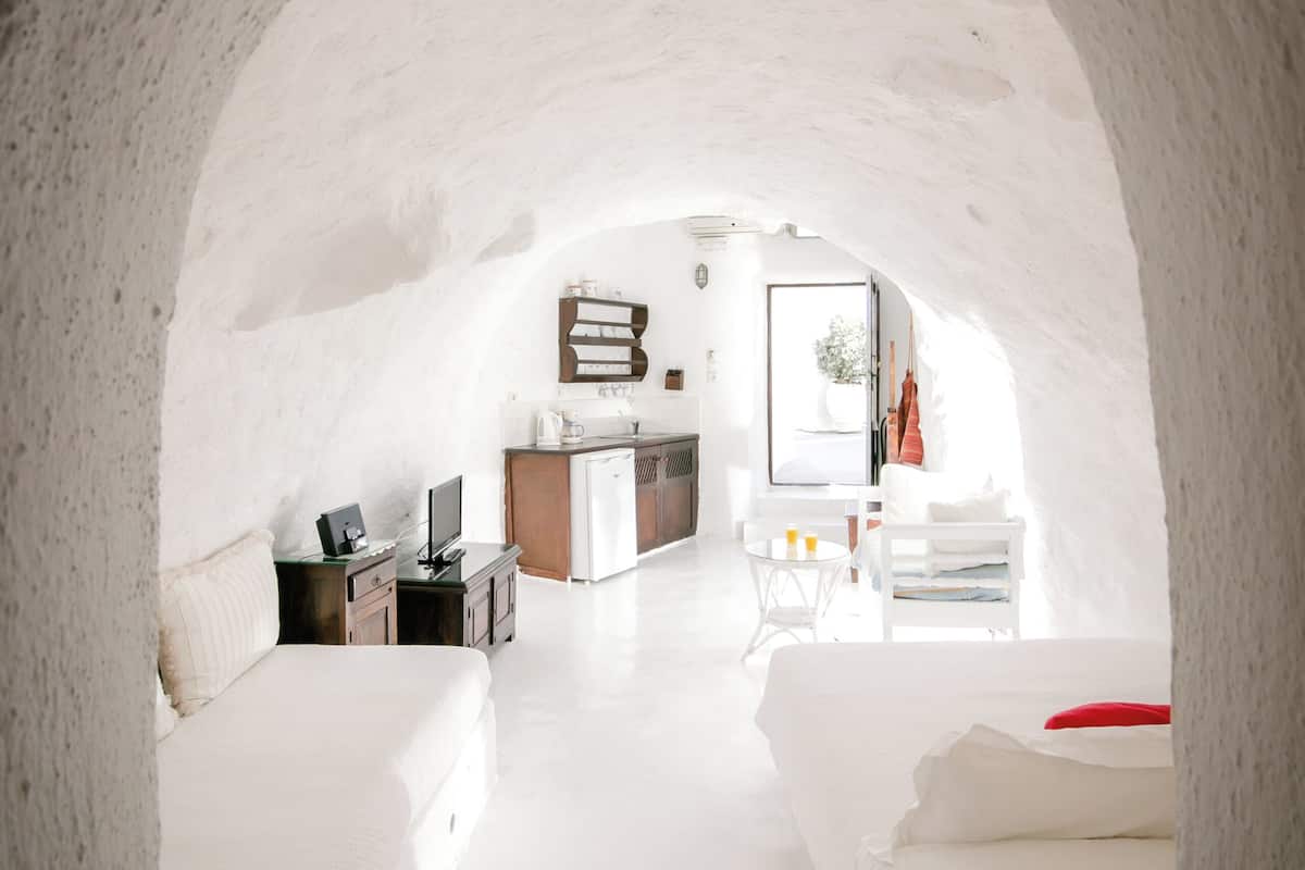 An arched, white-walled interior with a bed, a desk, and a small kitchenette.