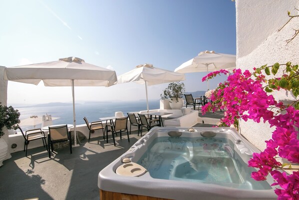 A rooftop terrace with a hot tub, white umbrellas, and outdoor seating.