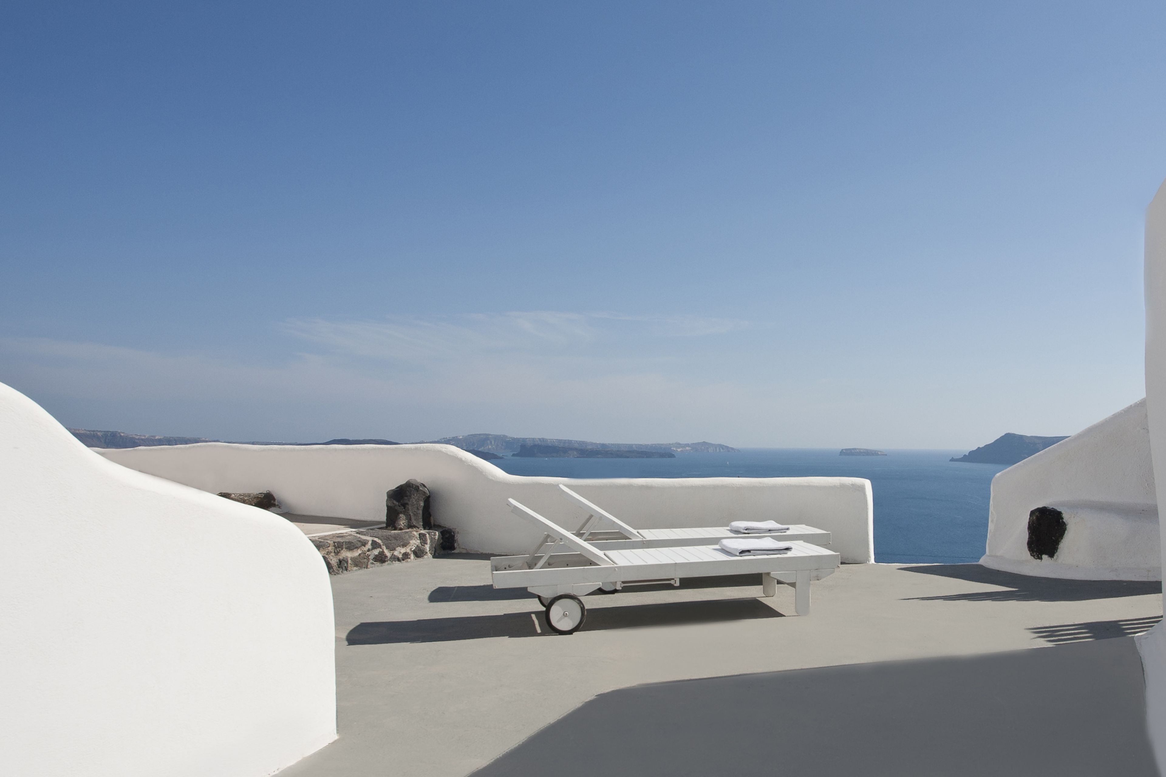 Une terrasse aux murs blancs, avec un fauteuil et une table, donnant sur la mer.