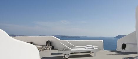 Une terrasse aux murs blancs, avec un fauteuil et une table, donnant sur la mer.