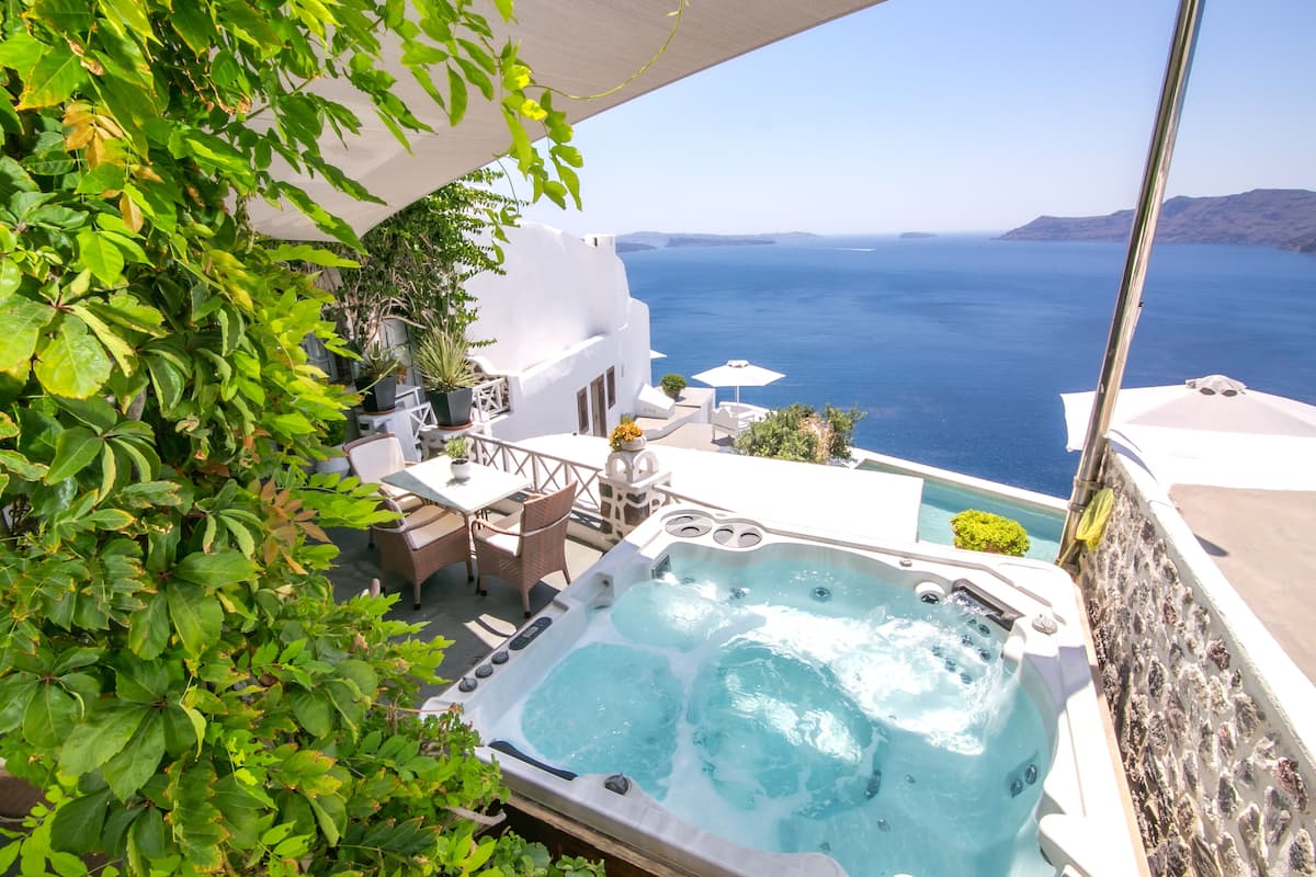 A hot tub with a view of the sea, outdoor seating, and a white building.